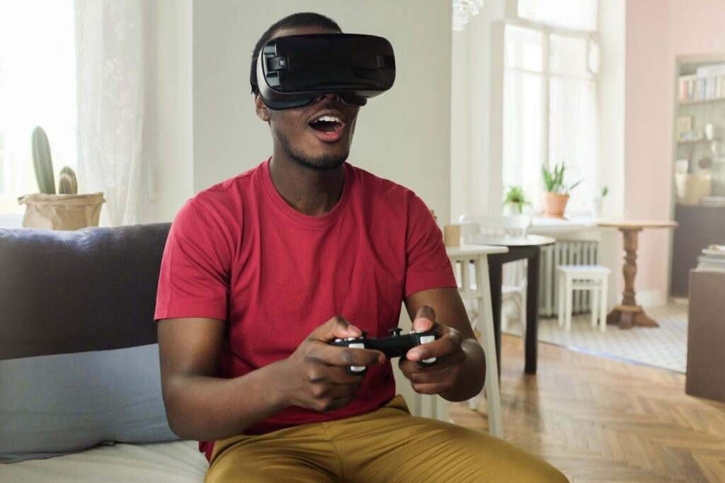Young African man in red T-shirt having rest on sofa with VR set on playing games