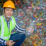 A male worker working at a recycling plant holds plastic bottles and tablets to dispose of and recycle plastic bottles at a small waste recycling plant