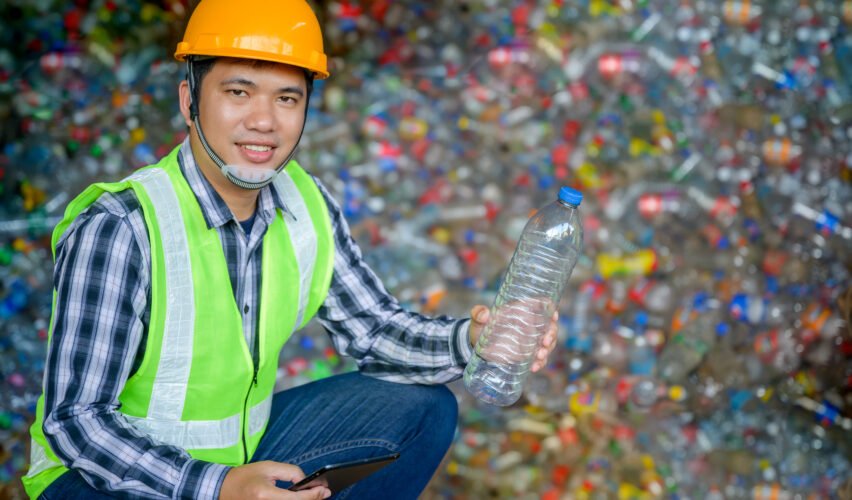 A male worker working at a recycling plant holds plastic bottles and tablets to dispose of and recycle plastic bottles at a small waste recycling plant